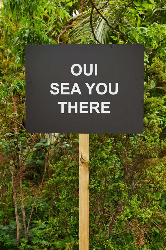Photo d'un détail de l’œuvre, un panneau avec l'inscription en anglais "OUI SEA YOU THERE"